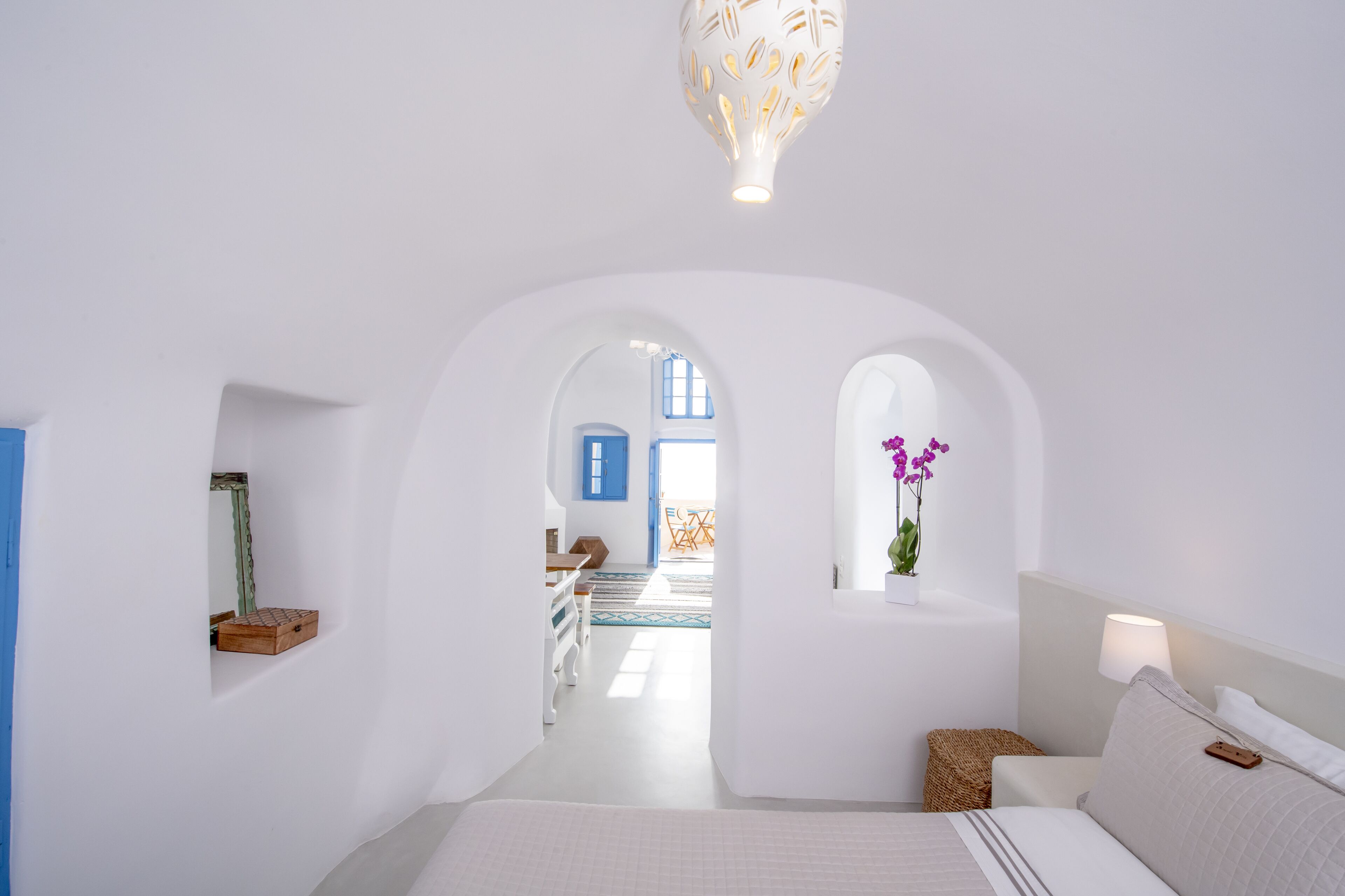 Quarto de paredes brancas com uma cama, um lustre e vista para outro cômodo com uma porta azul.