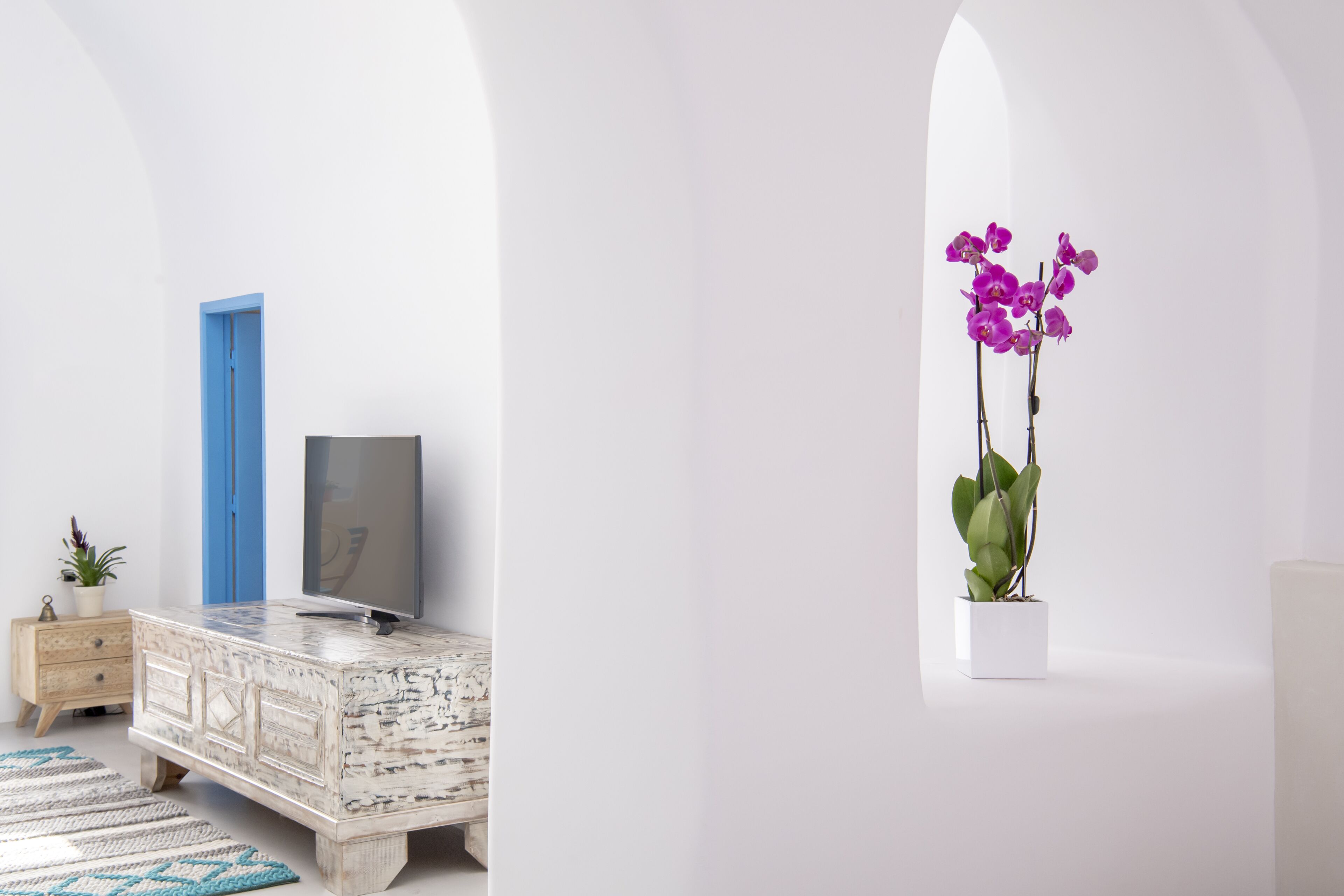 Una stanza minimalista con un mobile in marmo, una porta blu e un'orchidea in vaso.