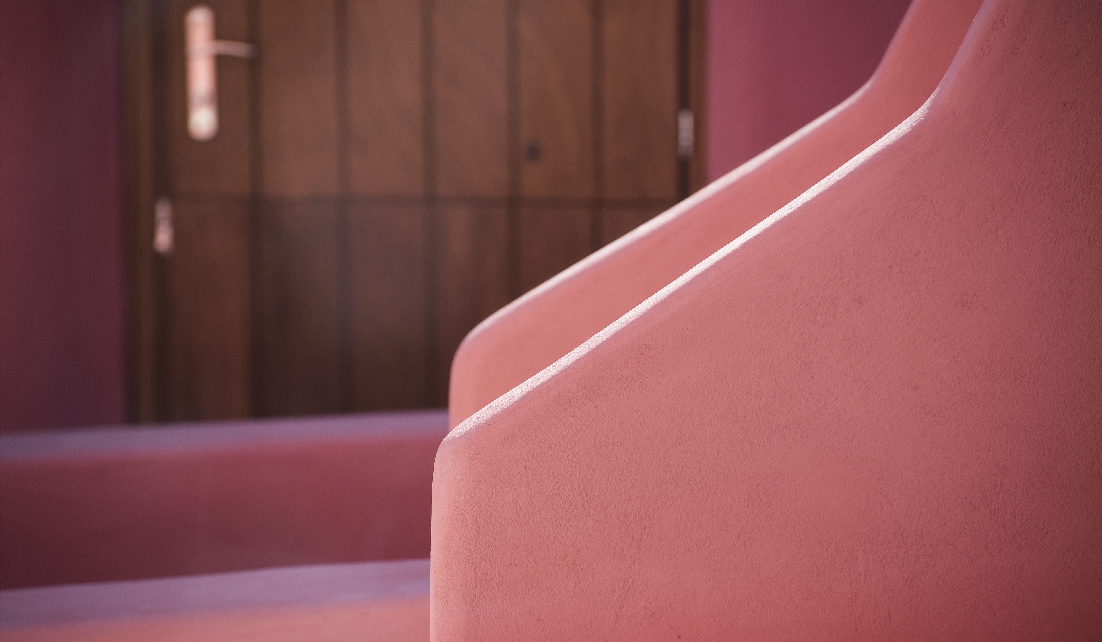 A close-up of a pink wall with a wooden door in the background.