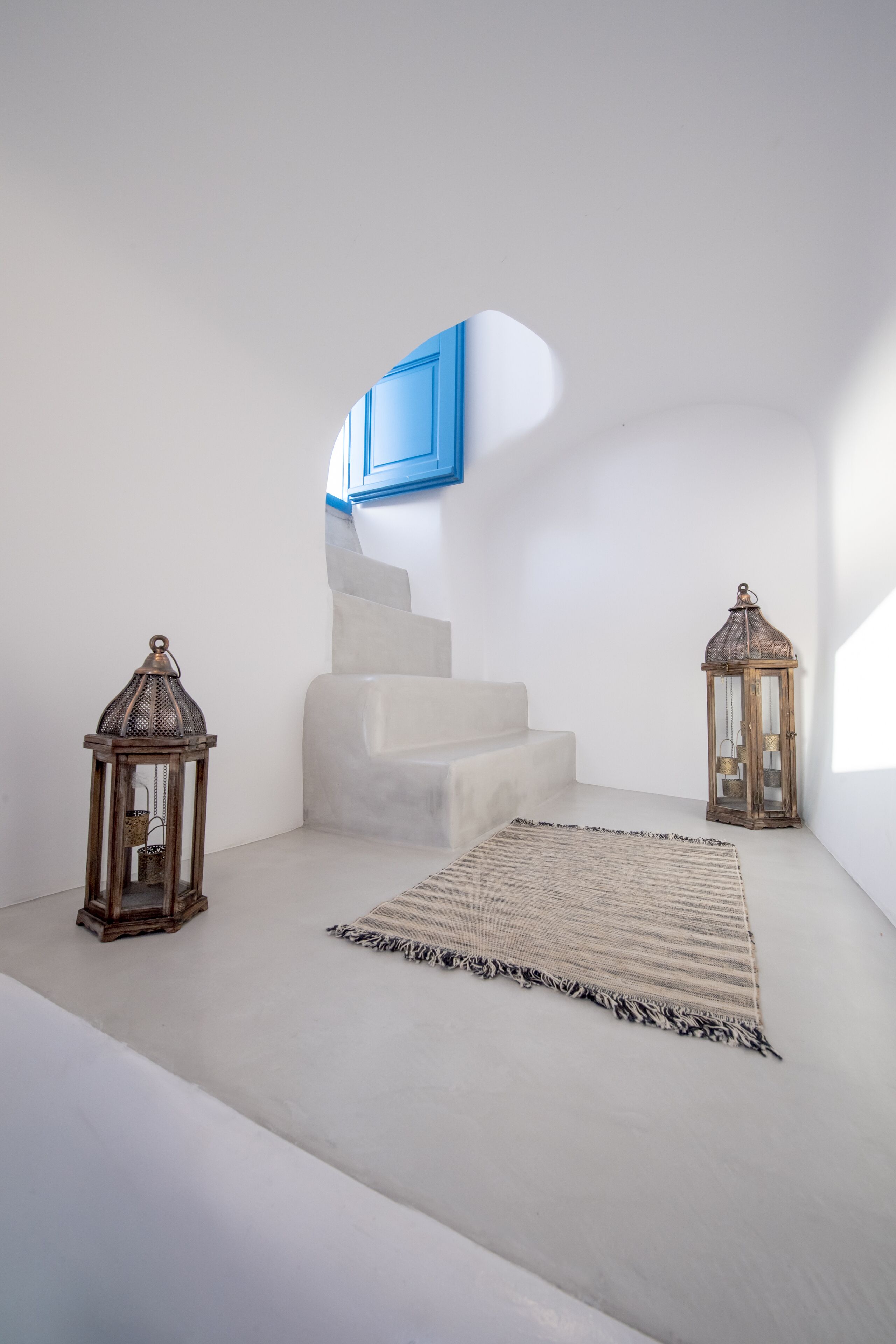 Habitación minimalista con una escalera blanca, dos faroles y una alfombra estampada.
