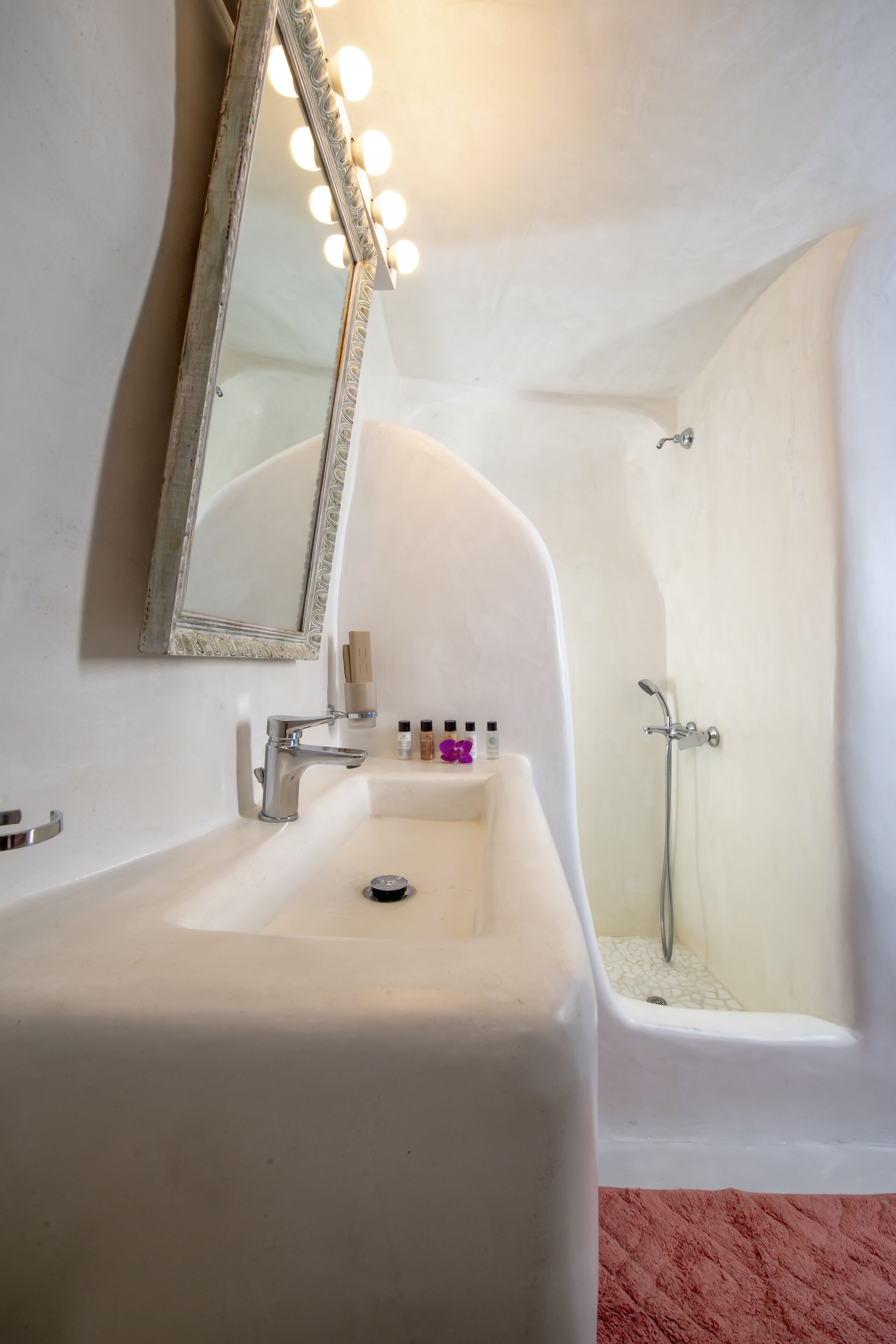 Un baño con un lavamanos blanco, un espejo con iluminación y una zona de ducha.
