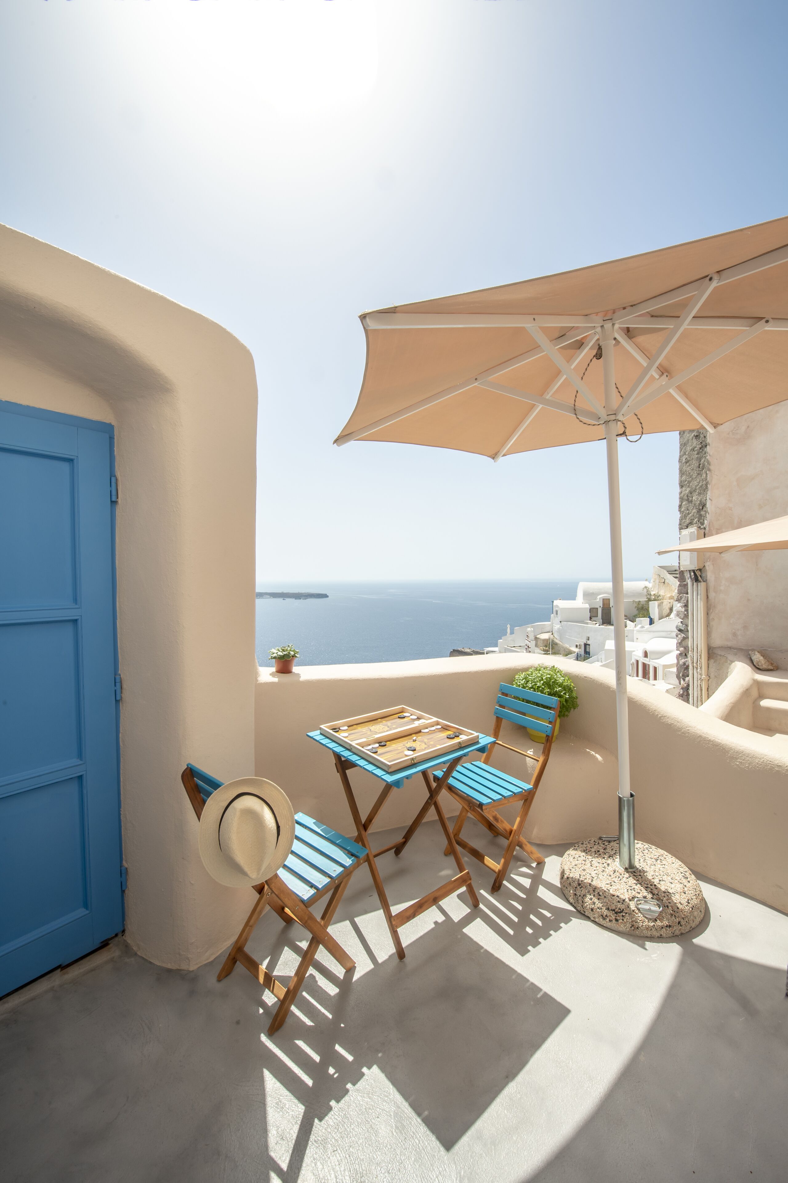 A balcony with a table and chairs, a blue door, and a view of the sea.