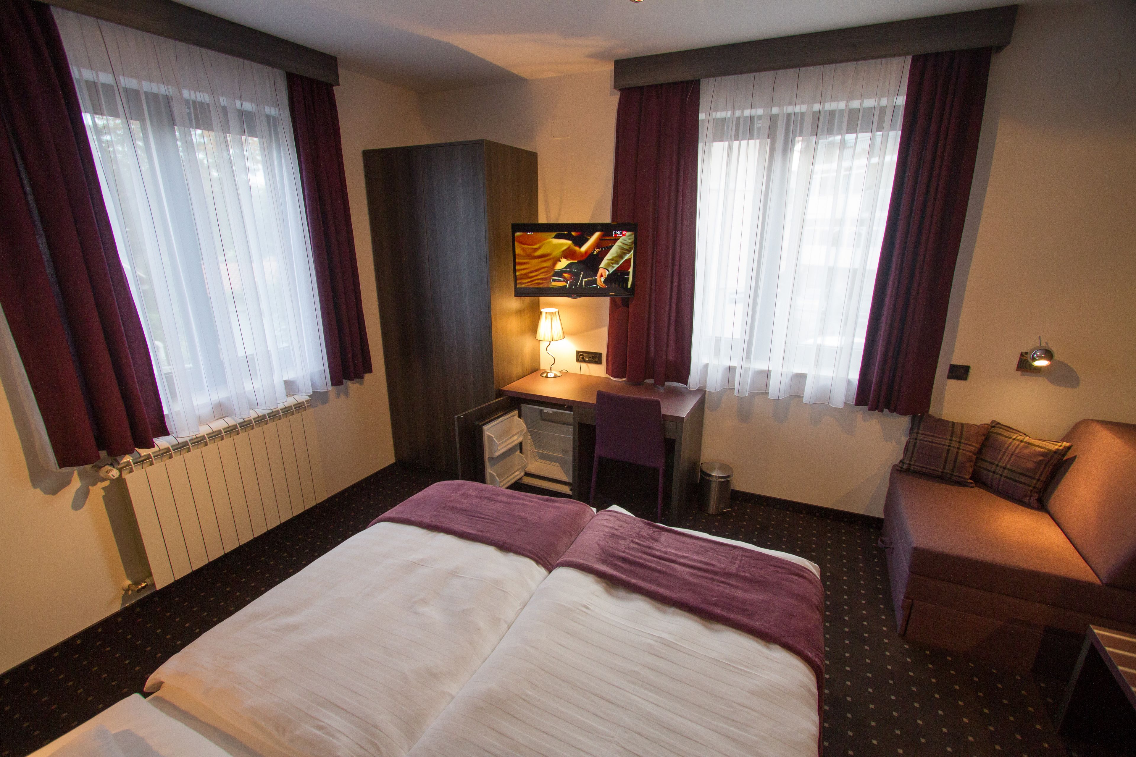 A hotel room with a bed, a desk, a television, and a sofa.