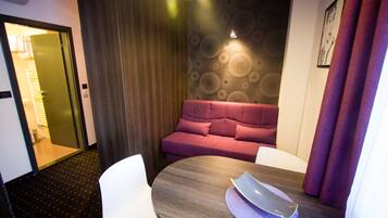 Een moderne hotelkamer met een houten tafel, witte stoelen, een rode bank en een behang met patroon.