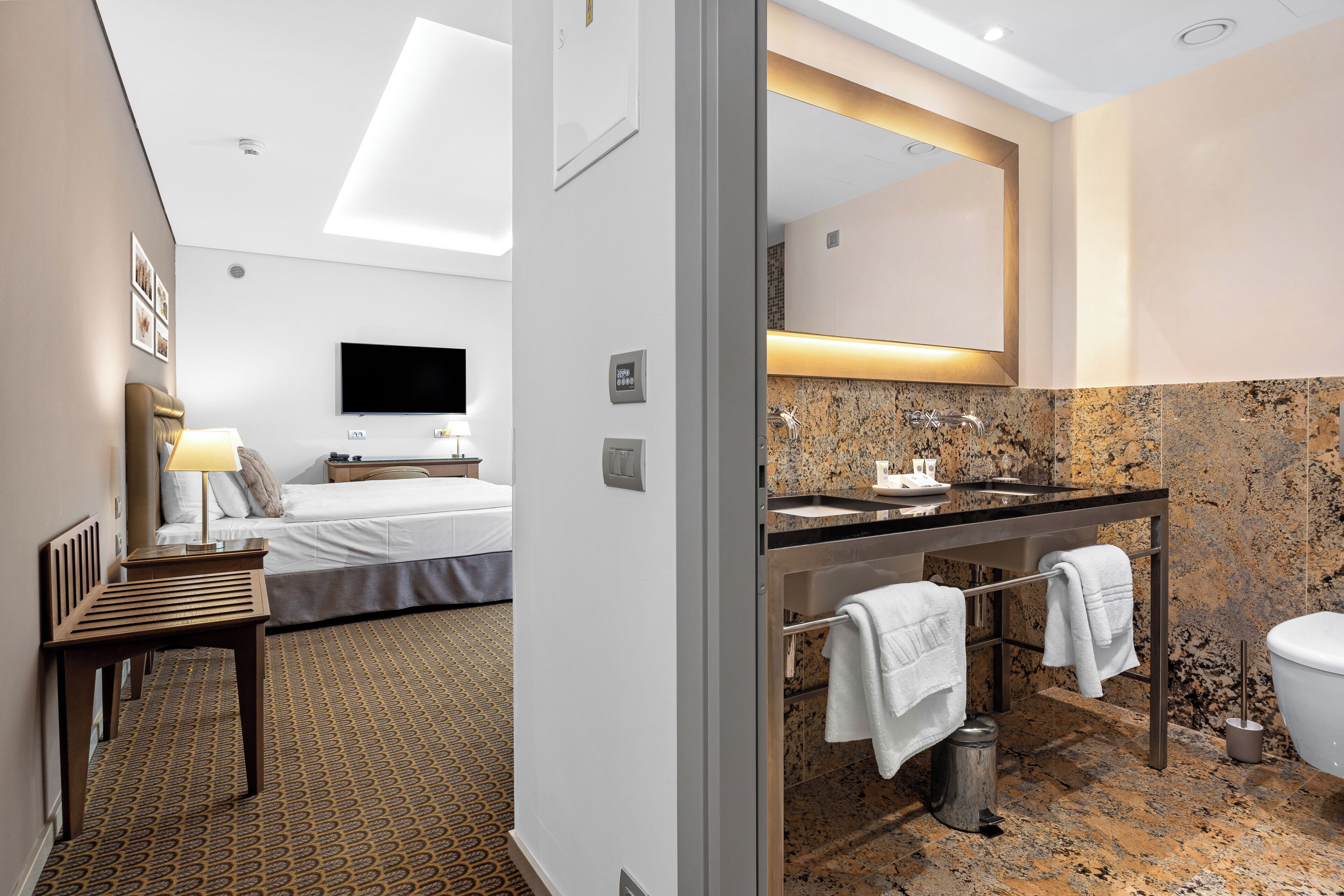 A hotel room with a bed, a desk, a TV, a bathroom with a sink, mirror, and toilet.