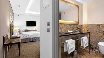 A hotel room with a bed, a desk, a TV, a bathroom with a sink, mirror, and toilet.