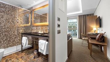 Un moderno baño de hotel con pared de mosaicos, ducha con cerramiento de vidrio, tocador con lavabo y espejo.