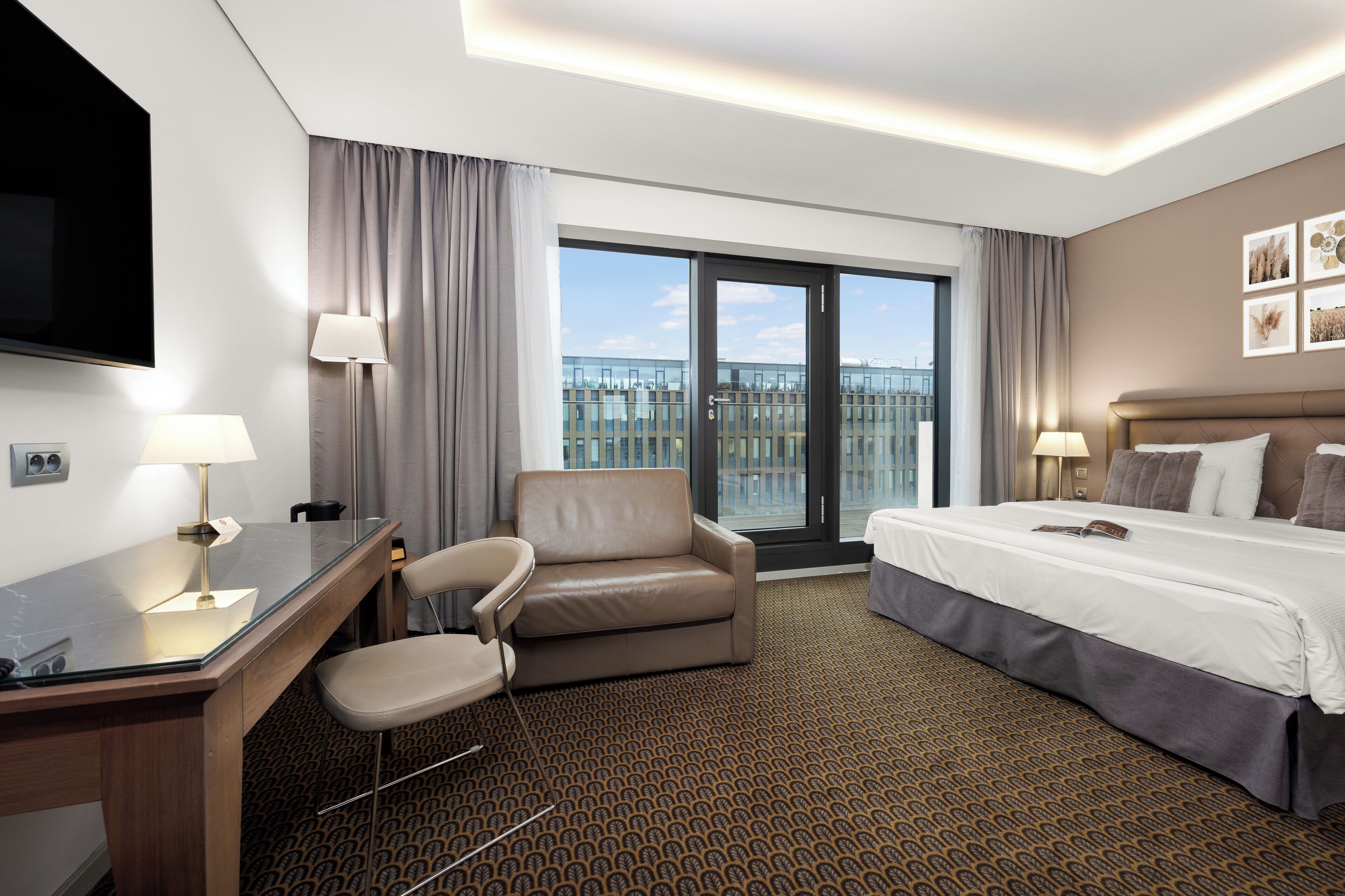 Habitación de hotel con cama, escritorio, silla y un amplio ventanal con vista a la ciudad.