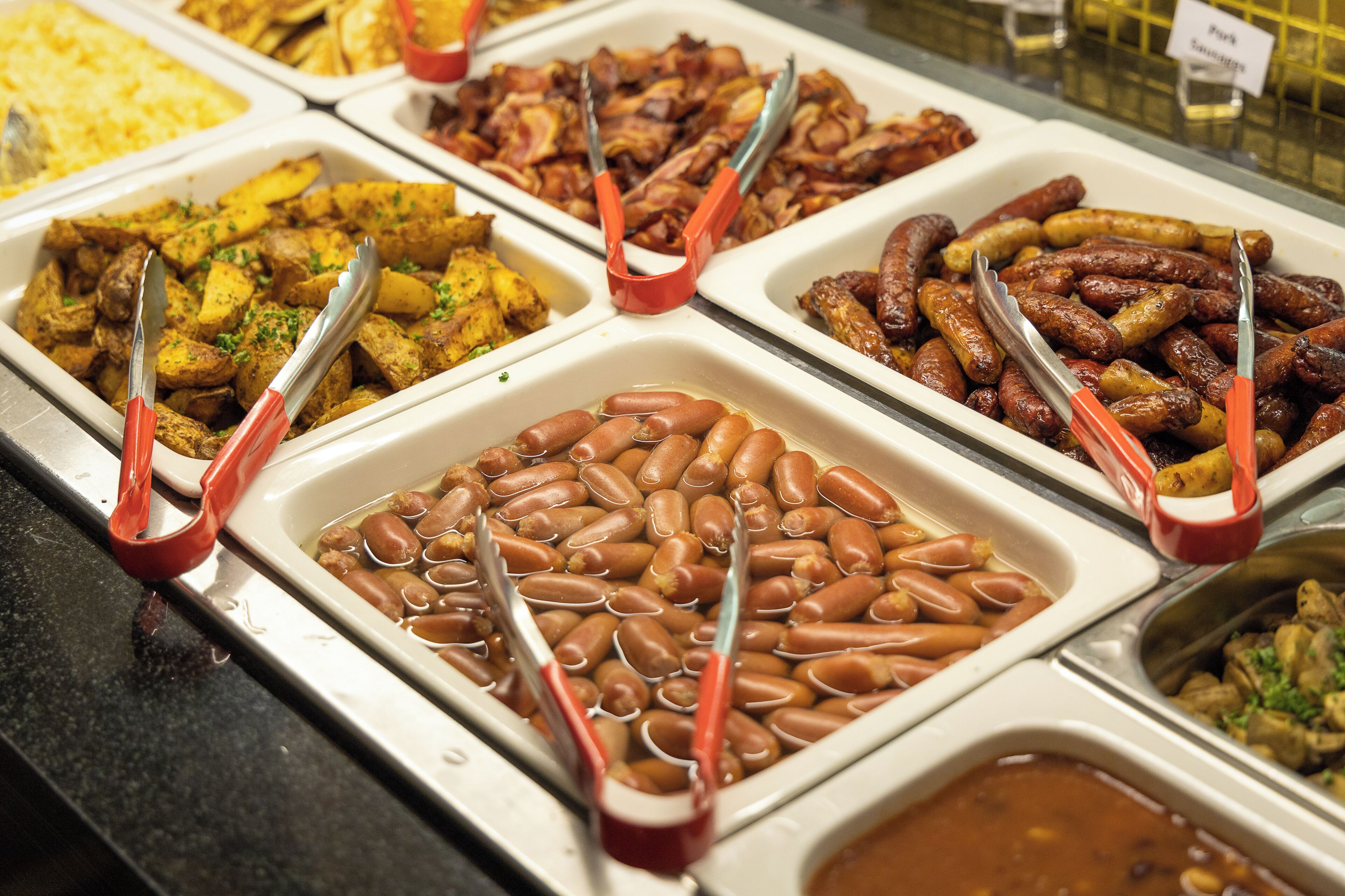 A buffet with various food options including potatoes, sausages, and beans.