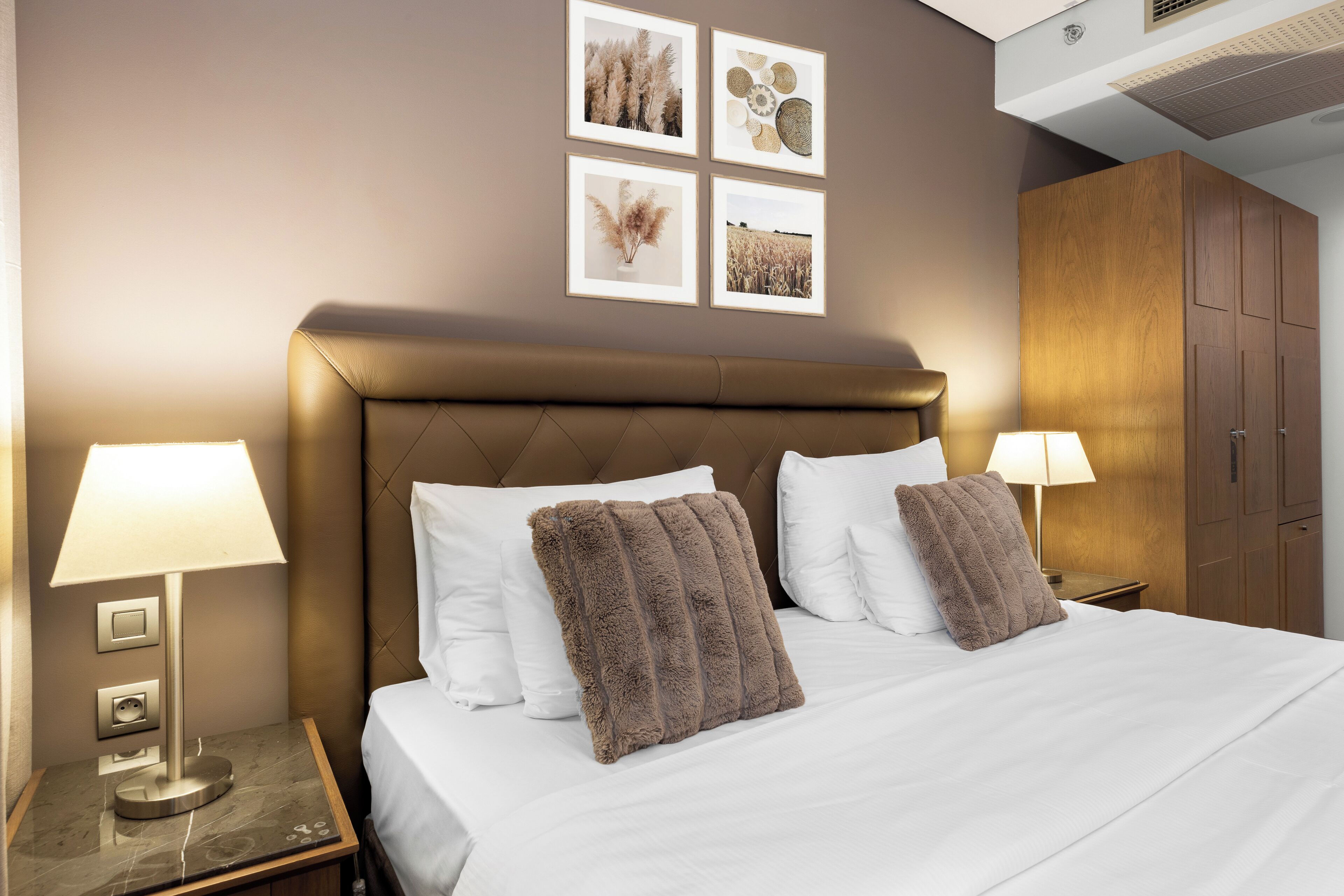 A hotel room with a bed, two bedside lamps, a nightstand, and a wardrobe.