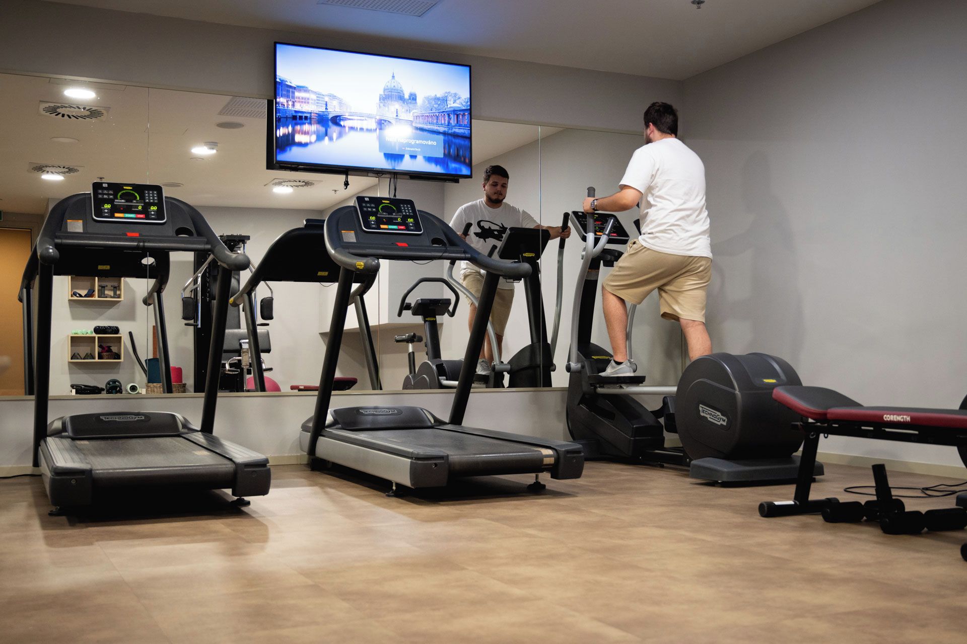 Ein Fitnessraum mit Laufbändern, einem Ergometer und einem Fernseher, der ein Programm zeigt.