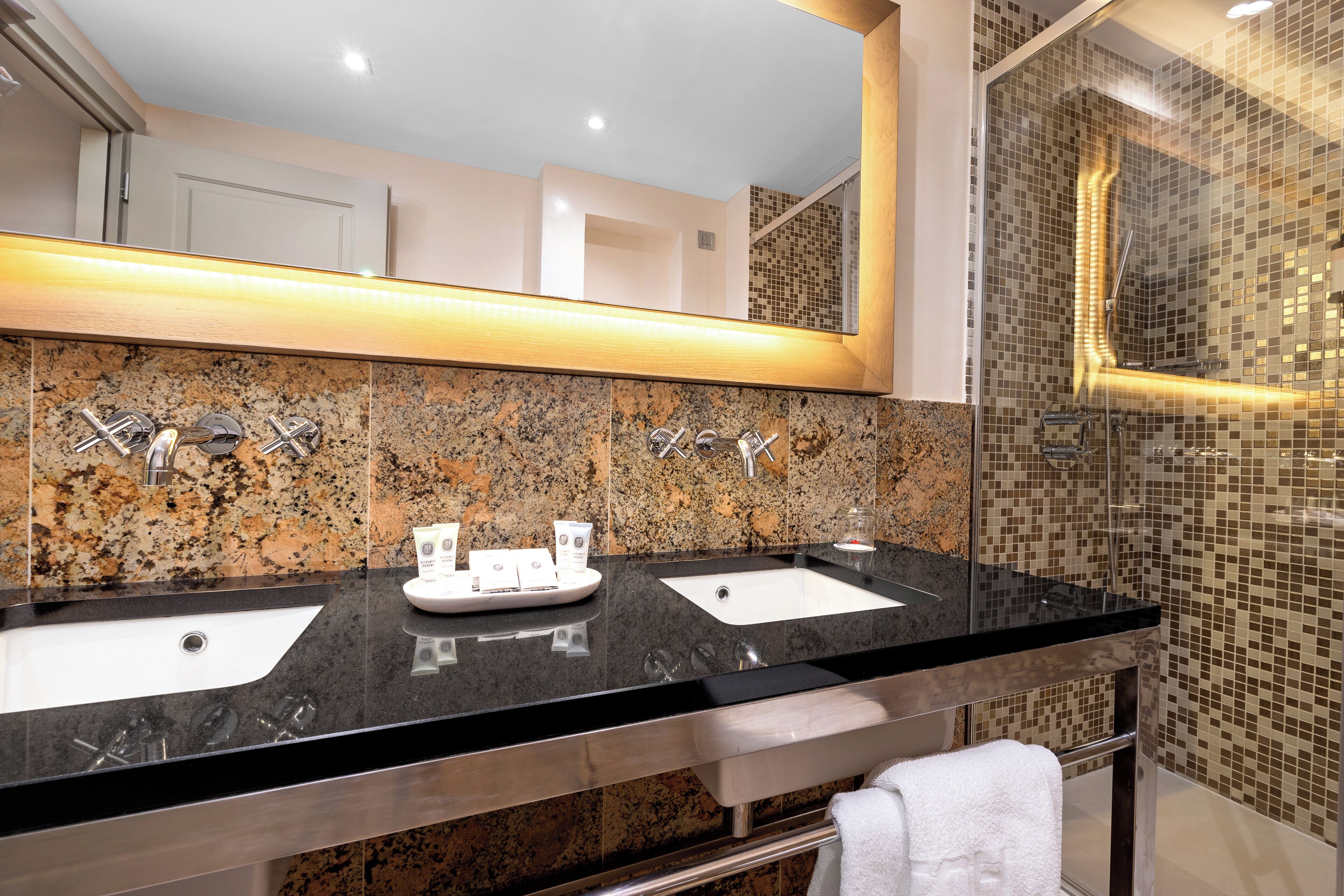 A bathroom with two sinks, a large mirror, and a shower area with mosaic tiles.