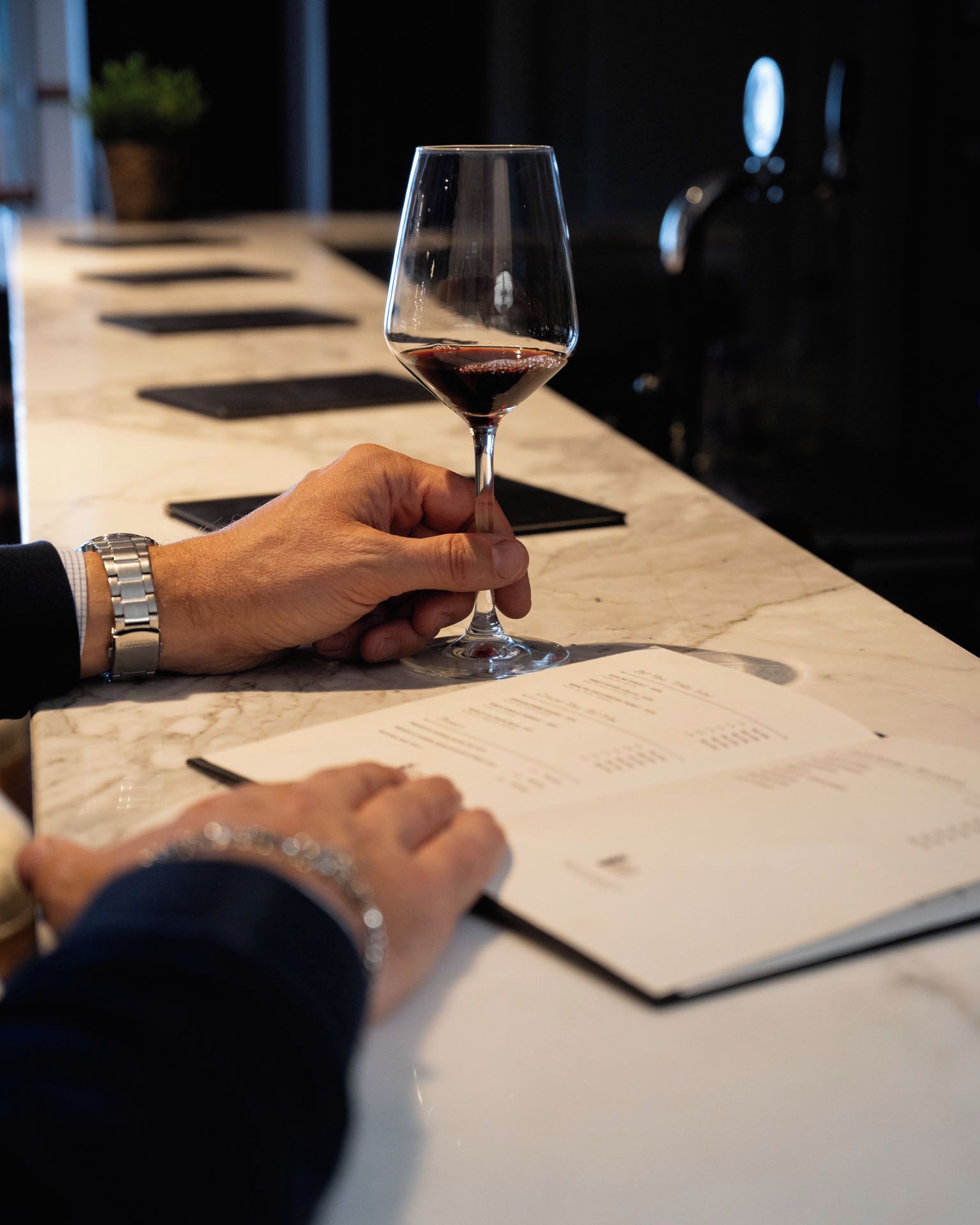 A person holding a wine glass, with a menu and a bottle in the background.