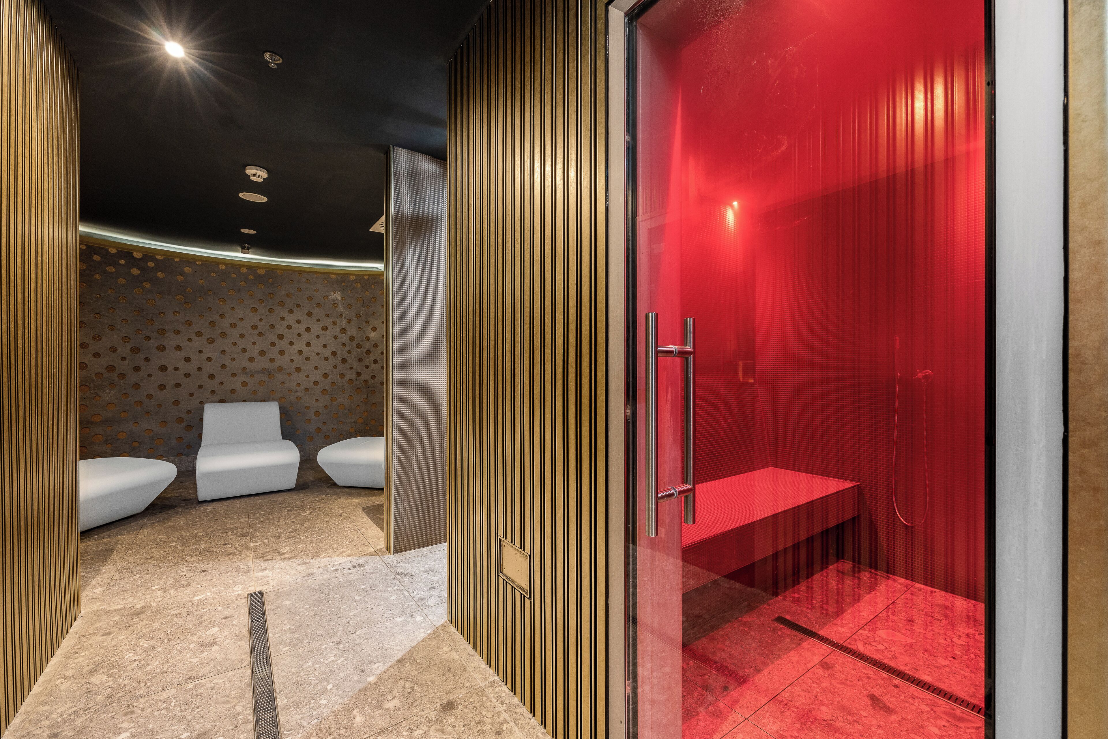 A modern spa area with a red-tiled floor, a glass-enclosed shower, and white seating.