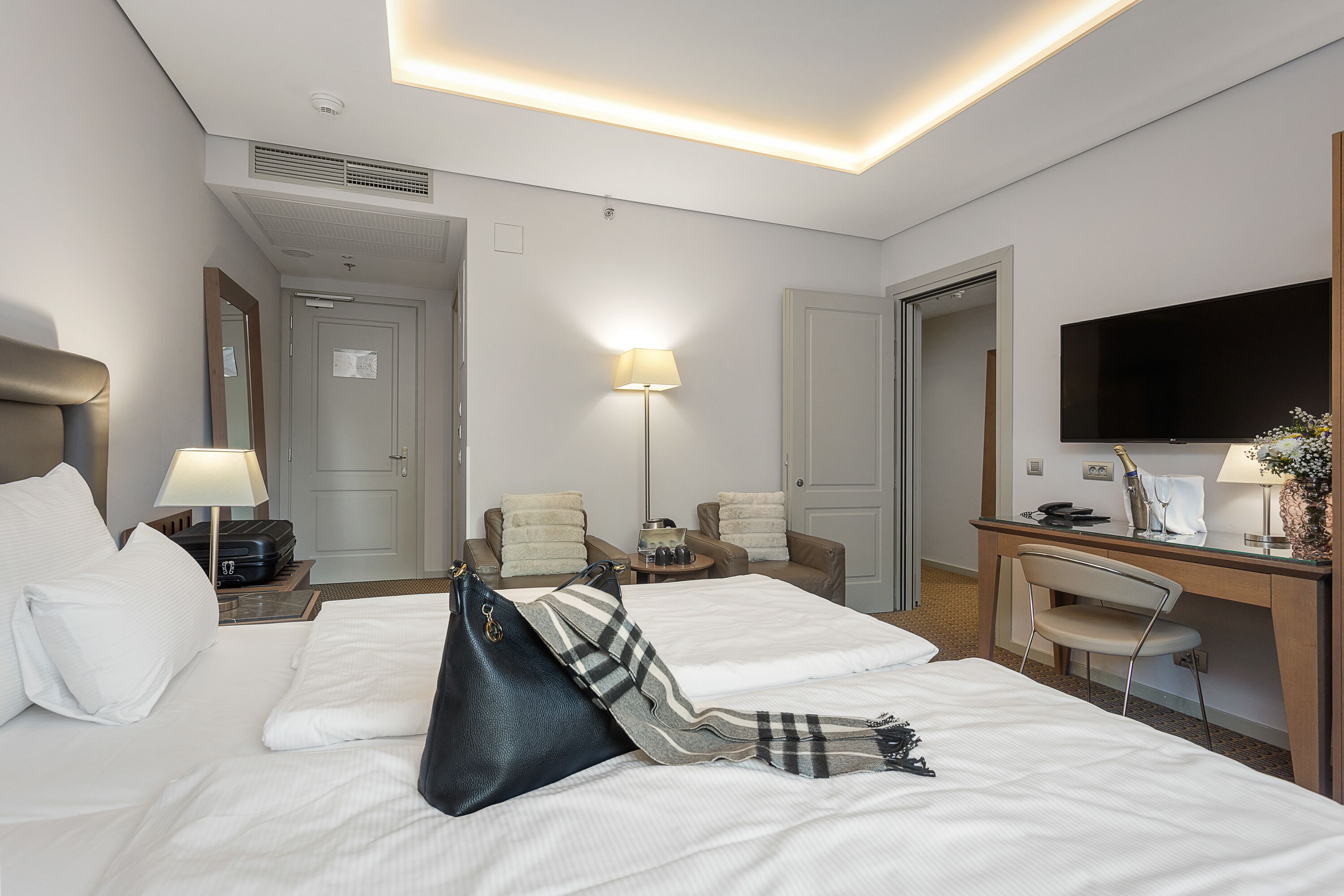 A hotel room with two beds, a desk with a chair, a TV, and a lamp.