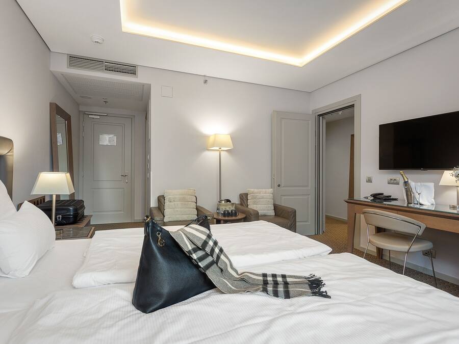 A hotel room with two beds, a desk with a chair, a TV, and a lamp.
