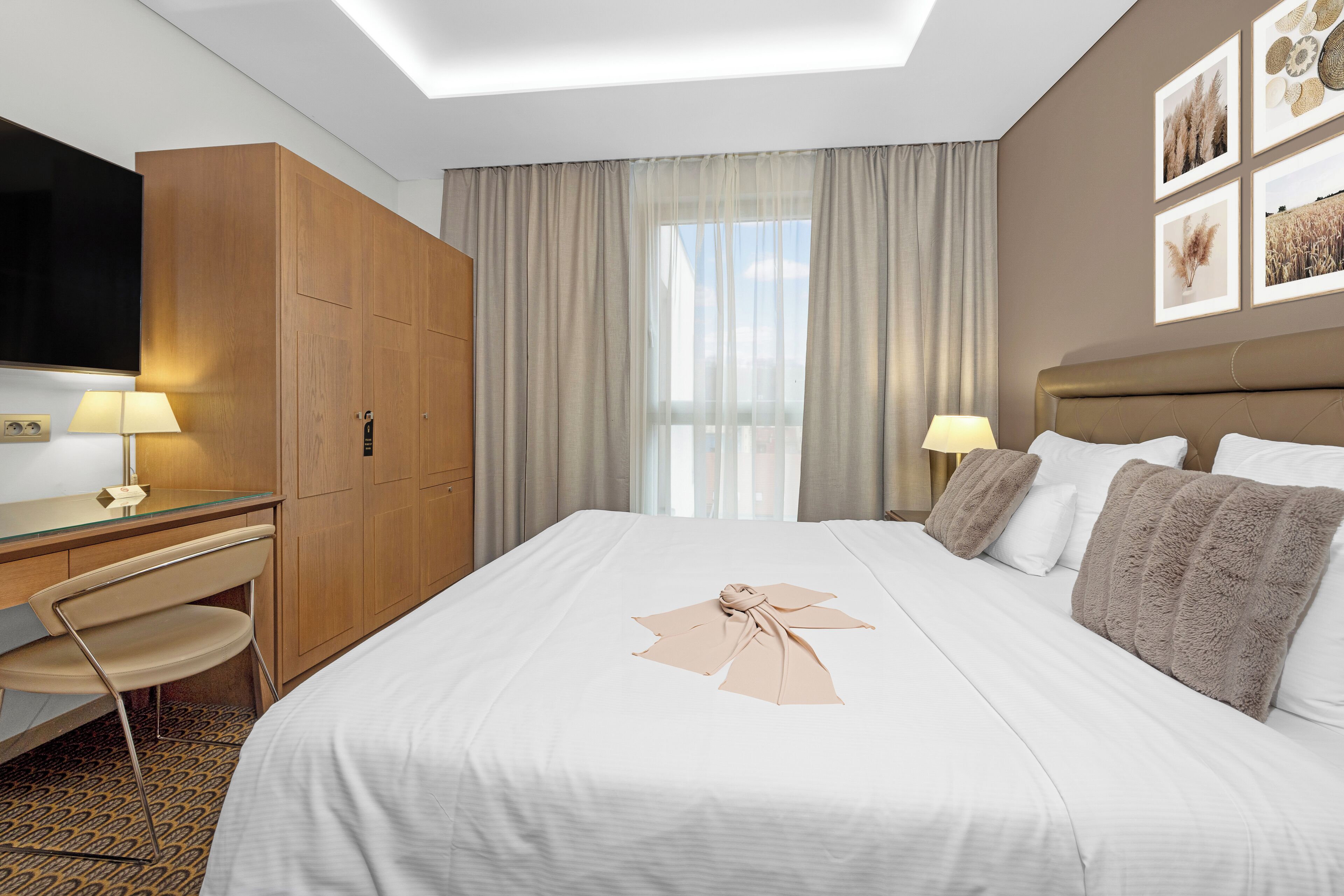 Una habitación de hotel con cama, escritorio, silla, televisor y ventana con cortinas.