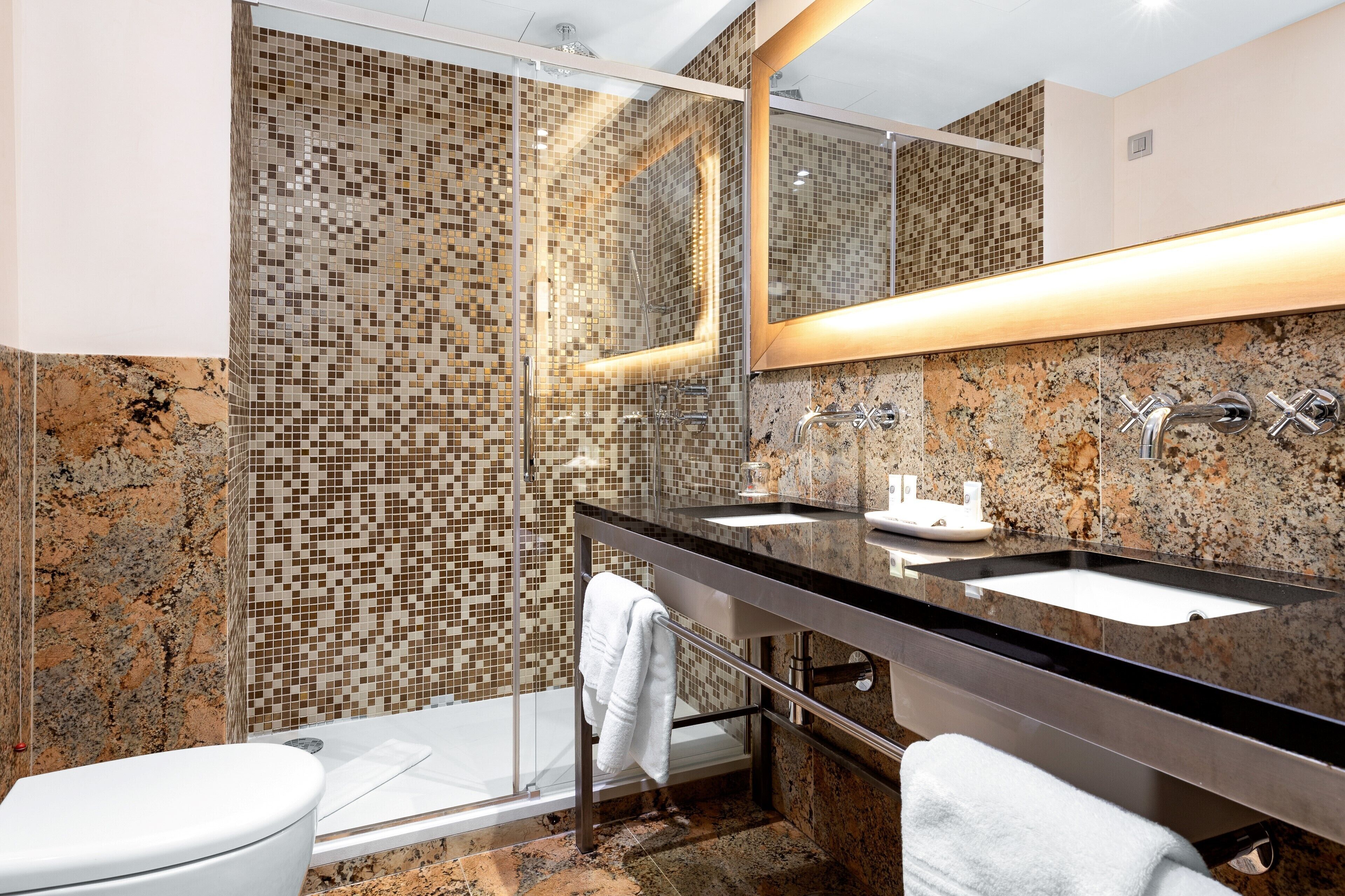 Un baño moderno con ducha de vidrio, encimera de granito y un espejo grande.