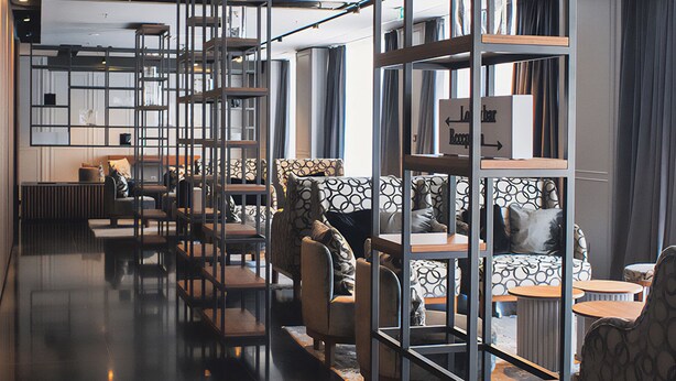 A modern interior with a sleek, reflective floor, a variety of seating options including sofas and chairs, and a central area with a wooden table and chairs. - Hotel Royal Prague (Prague)