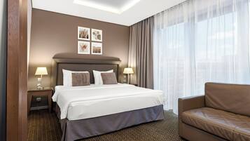 Una habitación de hotel con una cama grande, dos mesitas de noche con lámparas, un sofá marrón y una alfombra estampada.
