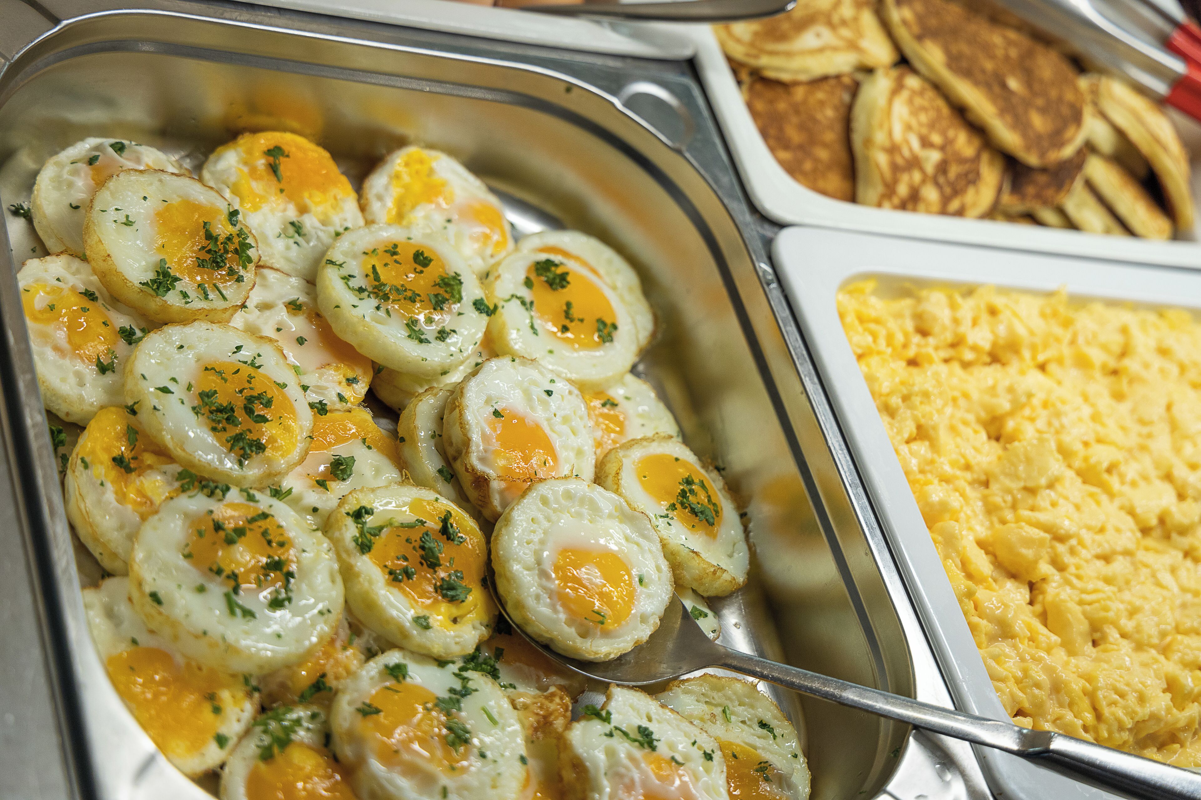 A buffet with various breakfast items including eggs, pancakes, and scrambled eggs.