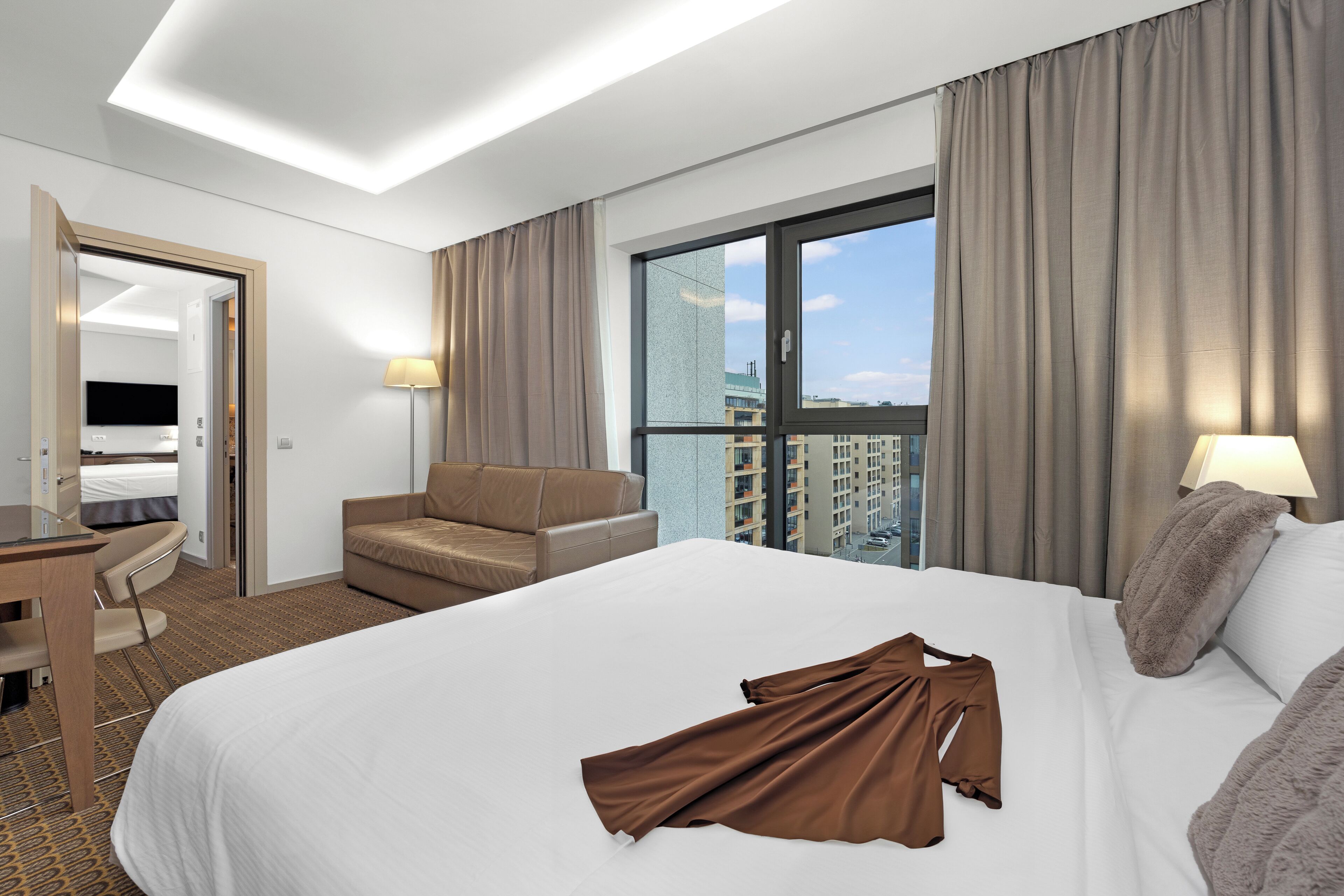 Een moderne hotelkamer met een groot bed, een bureau, een stoel en uitzicht op de stad door een groot raam.