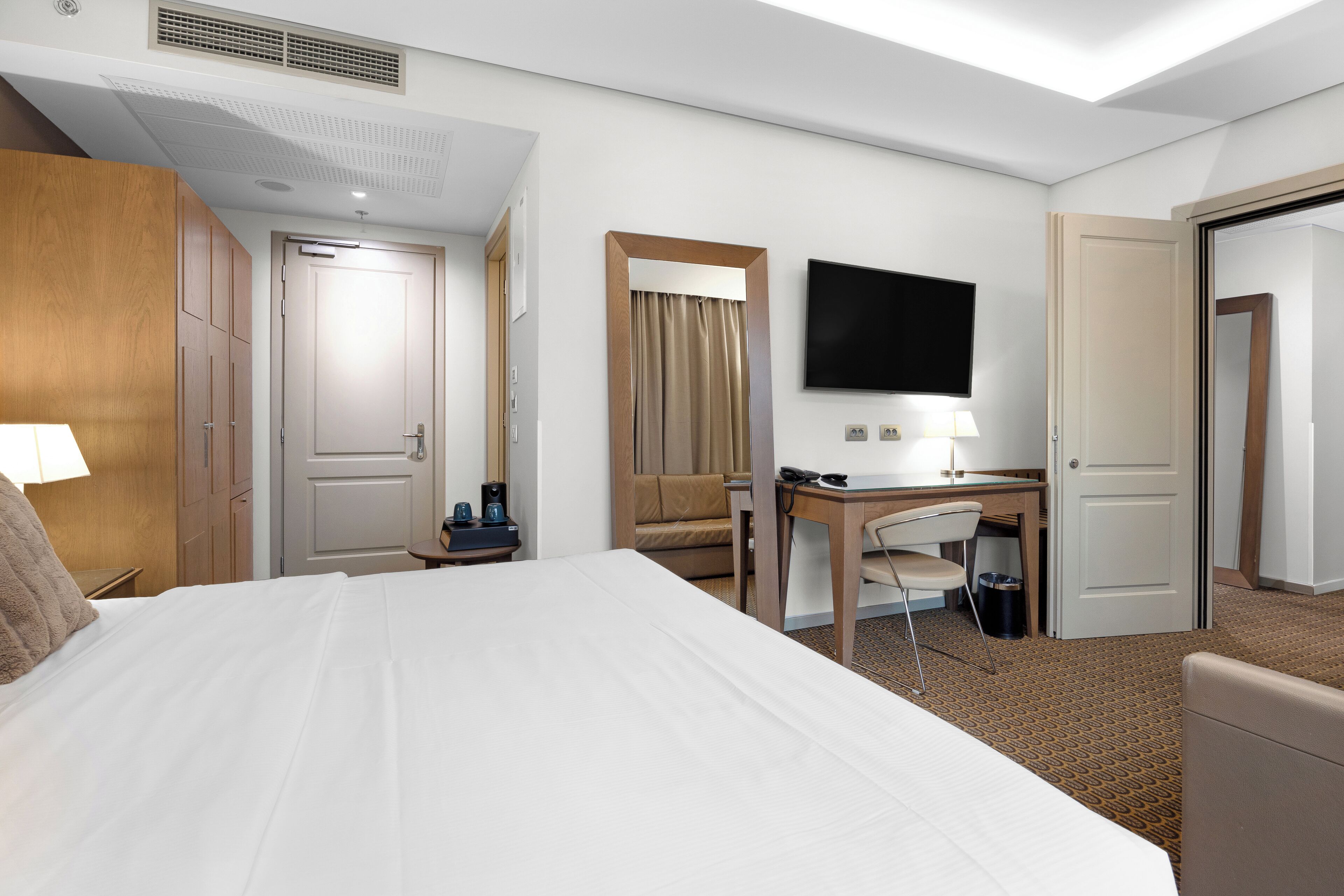 Ein Hotelzimmer mit einem großen Bett, einem Schreibtisch, einem Sessel, einem Fernseher und einem Kleiderschrank.