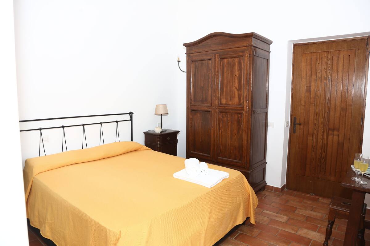 A room with a bed, wooden wardrobe, and a table with glasses.