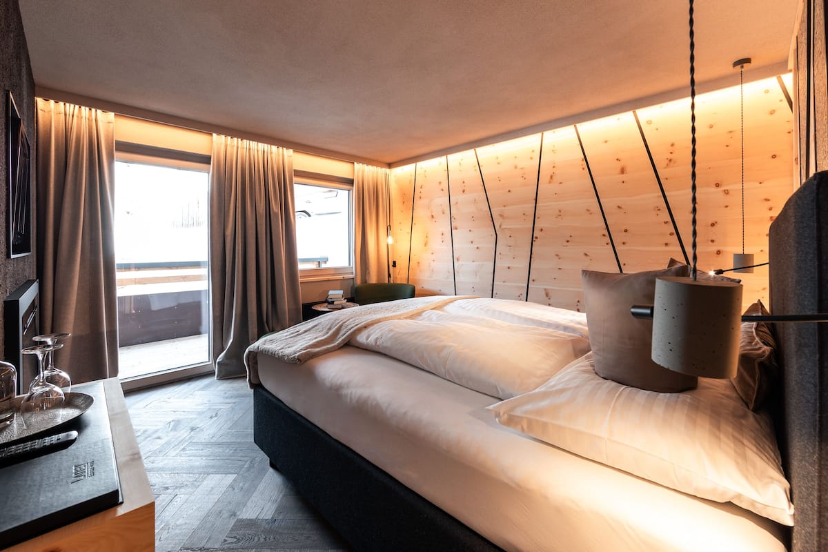 Habitación de hotel moderna con una cama grande, una mesita de noche con lámpara, vistas de la ciudad por la ventana y suelo de madera.