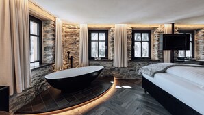 Un baño moderno con una bañera independiente, paredes de piedra y ventanas amplias.