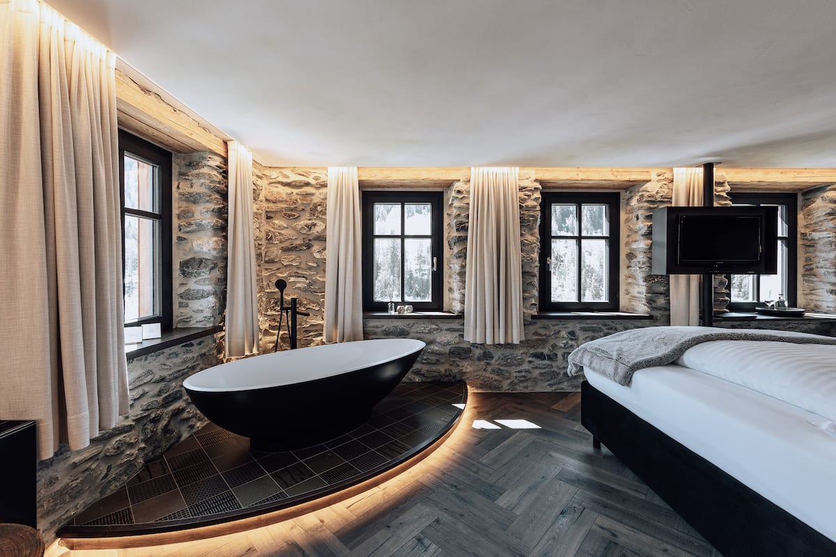 Un baño moderno con una bañera independiente, paredes de piedra y ventanas amplias.