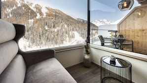 Una habitación moderna con un gran ventanal que ofrece vistas a una montaña nevada, un comedor de madera y una zona de estar acogedora.