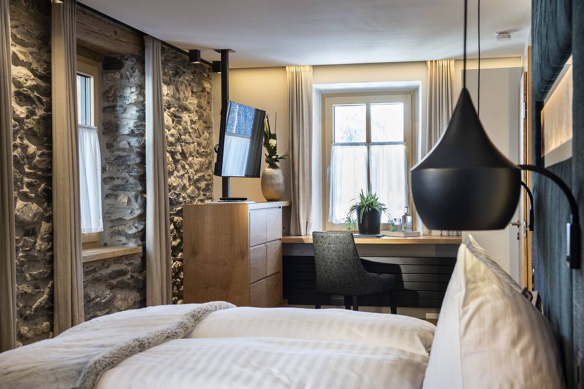 Un dormitorio con cama, escritorio, silla, televisor y pared de piedra.
