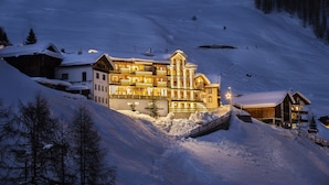 Un hotel grande de varios pisos con techo nevado e iluminación exterior, situado en una pendiente cubierta de nieve.