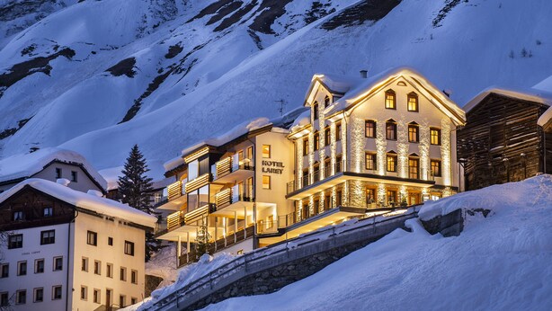Un hotel de varios pisos con balcones y una montaña nevada al fondo.