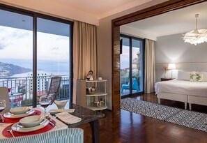 Une chambre d’hôtel avec balcon, un coin repas avec une table dressée pour deux personnes, et un lit donnant sur la ville.