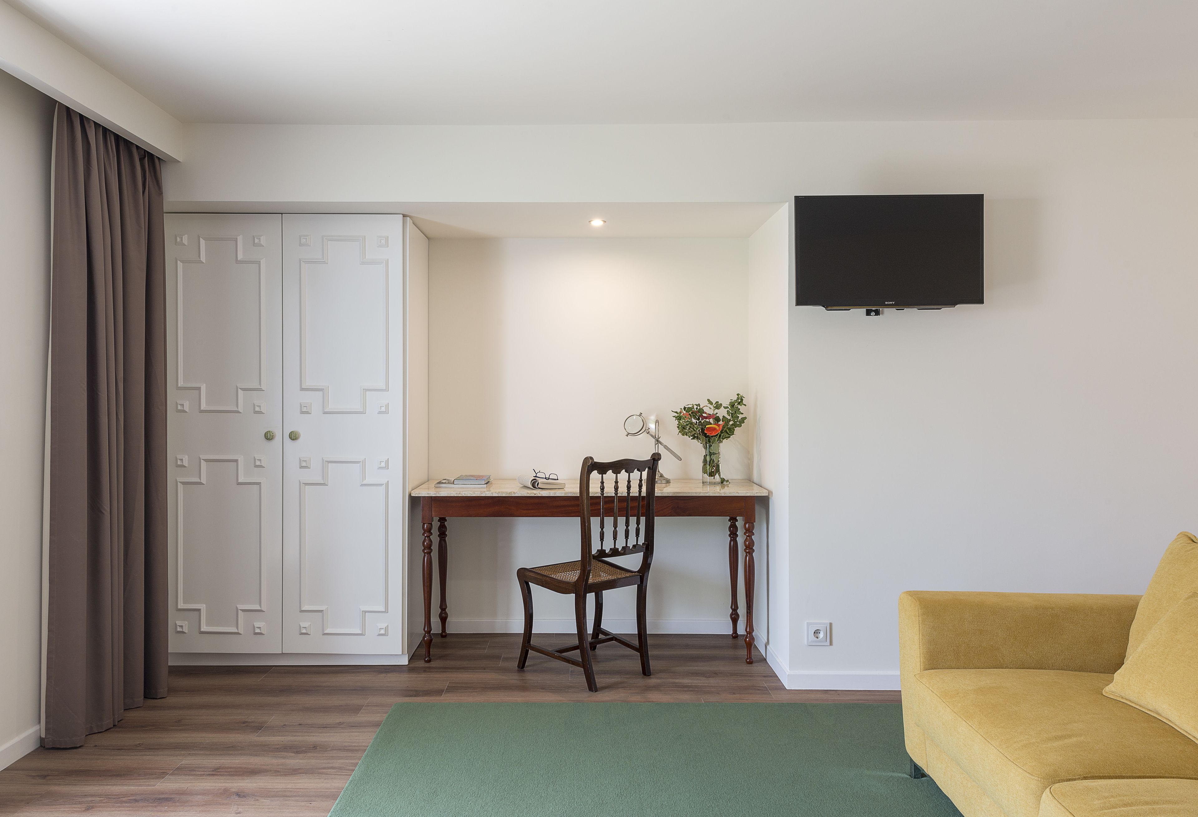 A room with a desk, chair, TV, wardrobe, and a yellow sofa.