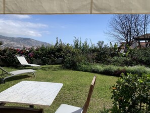 Un patio con una mesa y sillas, un área verde y una vista de la ciudad y montañas al fondo.