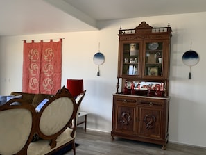 Ein Zimmer mit einem Holzschrank, einem roten Vorhang und einem Esstisch mit Stühlen.