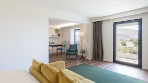 A modern hotel room with a large bed, a seating area with a sofa and chairs, a small dining table, and a view of the city through a large window. - Belvedere Boutique - Adults Only (Funchal)