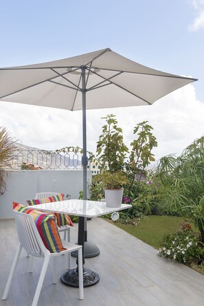 Un patio con una mesa, sillas, una sombrilla grande y plantas en macetas.