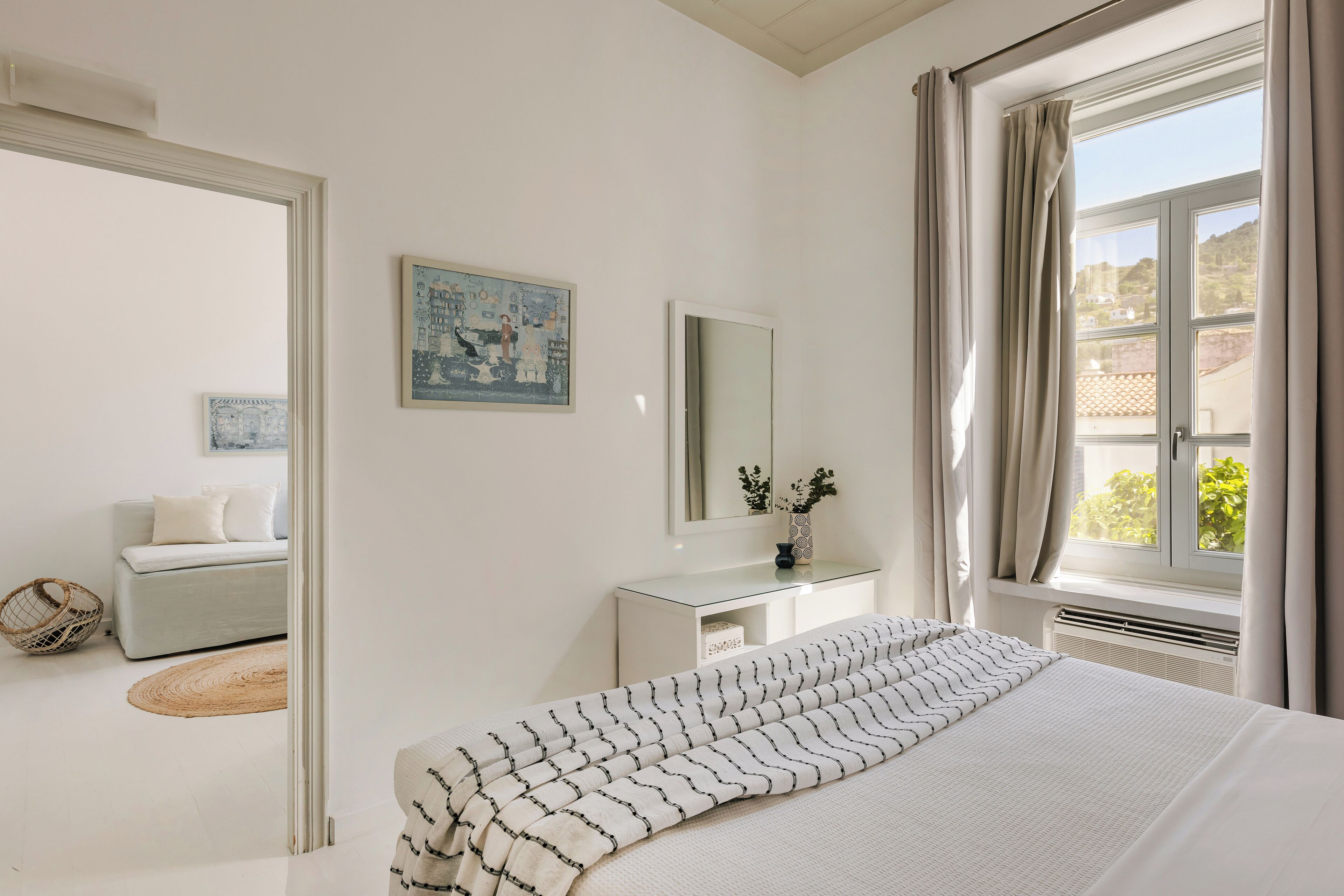 Un dormitorio con cama, mesita de noche, cómoda, espejo y ventana con cortinas.