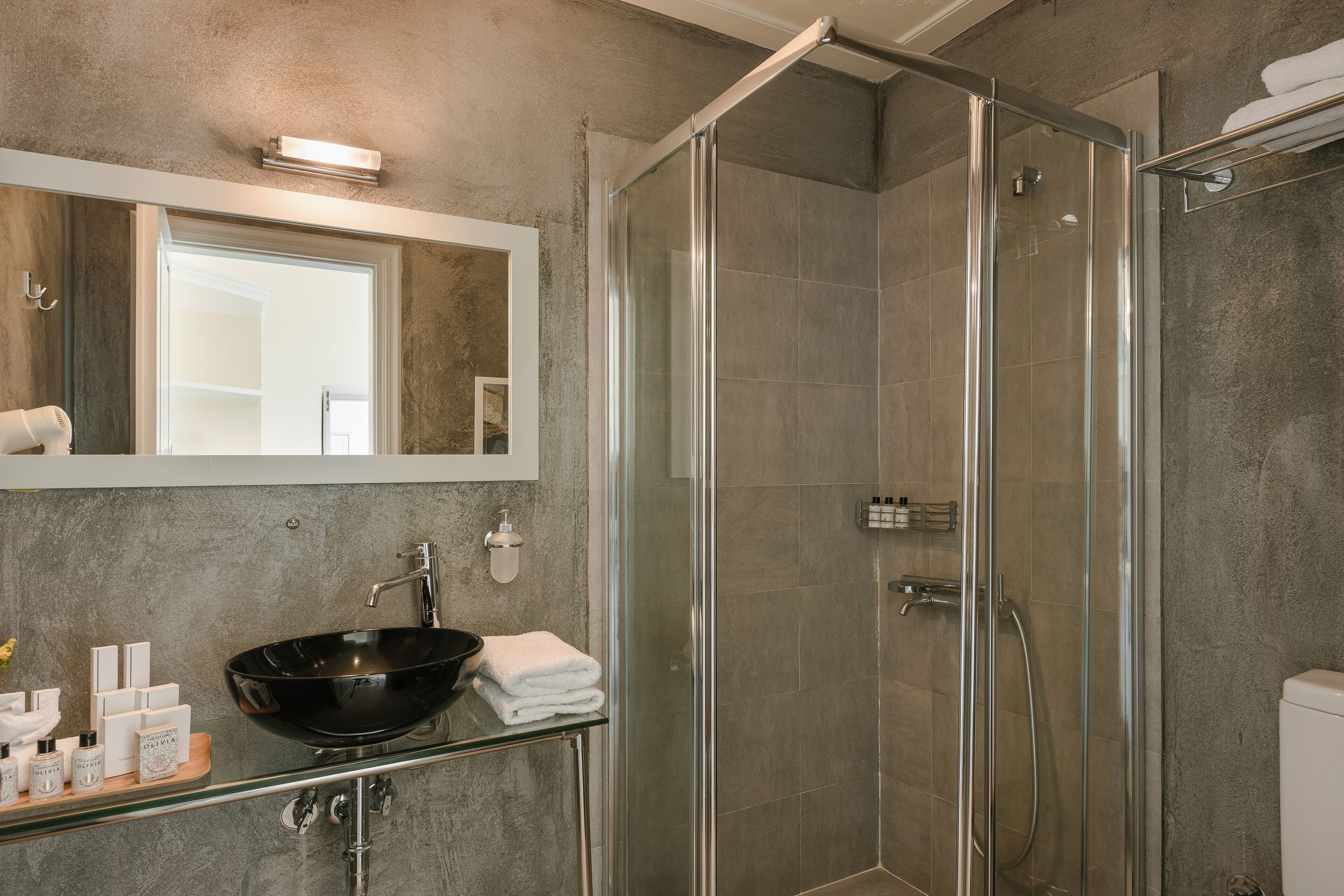 A modern bathroom with a glass-enclosed shower, a large mirror, and a glass sink with toiletries.