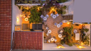 An outdoor patio with multiple seating areas, potted plants, and a tiled roof. - Hydra Hotel (Hydra)