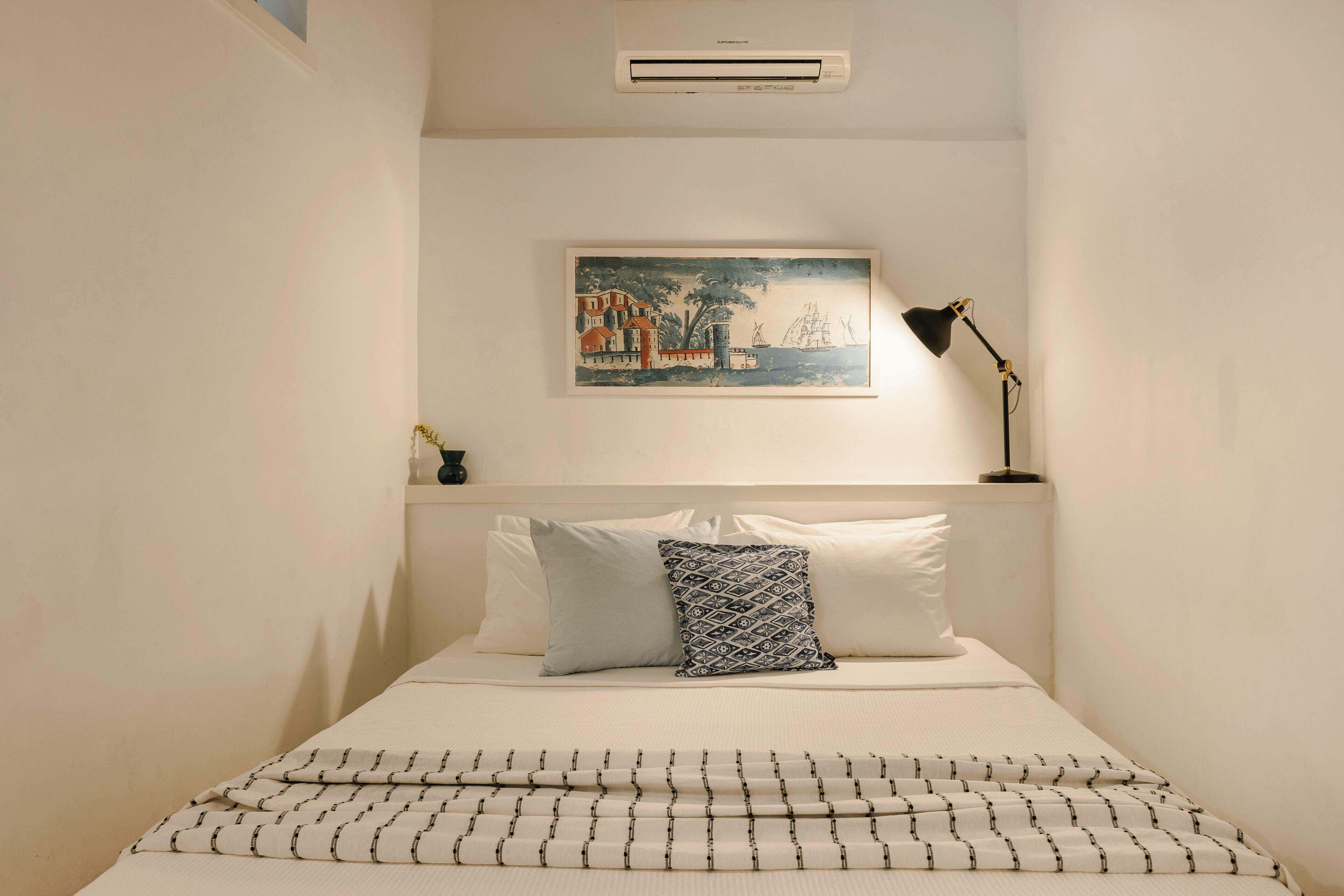 A neatly arranged bedroom with a bed, pillows, a framed artwork, and a floor lamp.