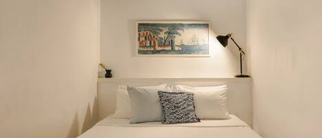 A neatly arranged bedroom with a bed, pillows, a framed artwork, and a floor lamp.