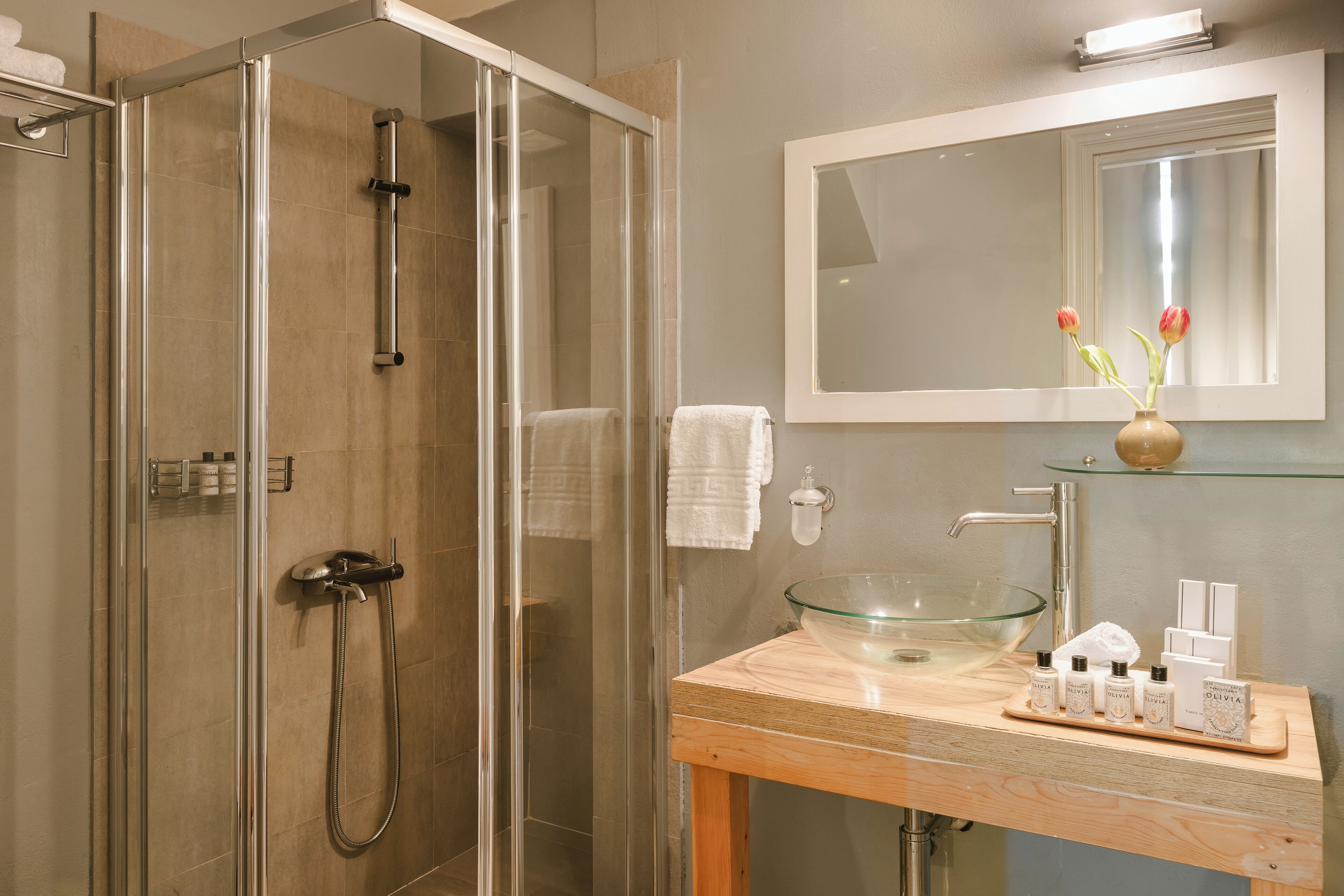 Un baño moderno con cabina de ducha de vidrio, tocador de madera y lavabo de vidrio, además de un espejo sobre el lavabo.