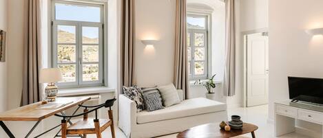 Una sala de estar moderna con un sofá, una mesa de madera, un televisor y ventanas grandes con cortinas.