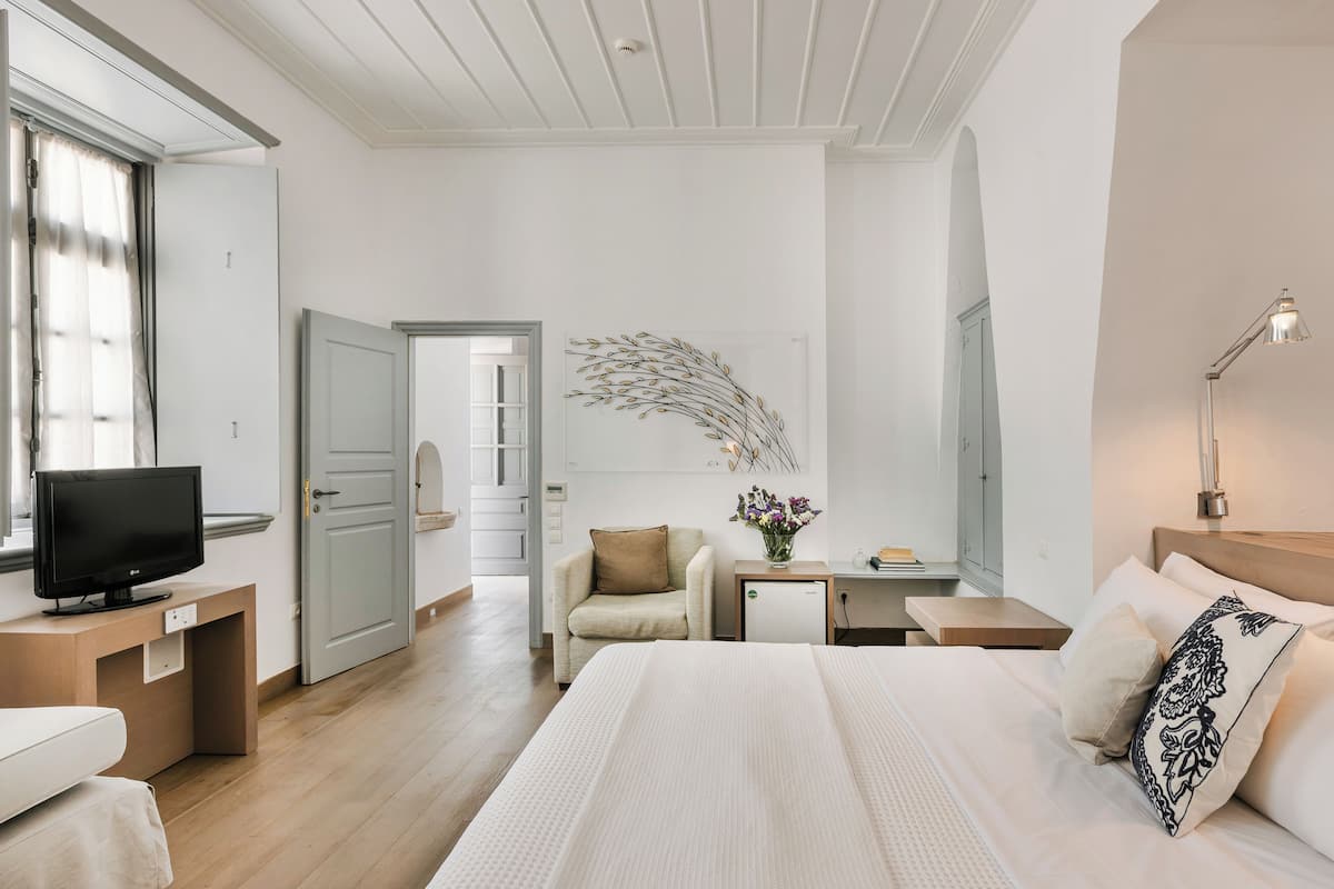 A hotel room with a bed, a desk, a TV, a chair, and a small table with a lamp.