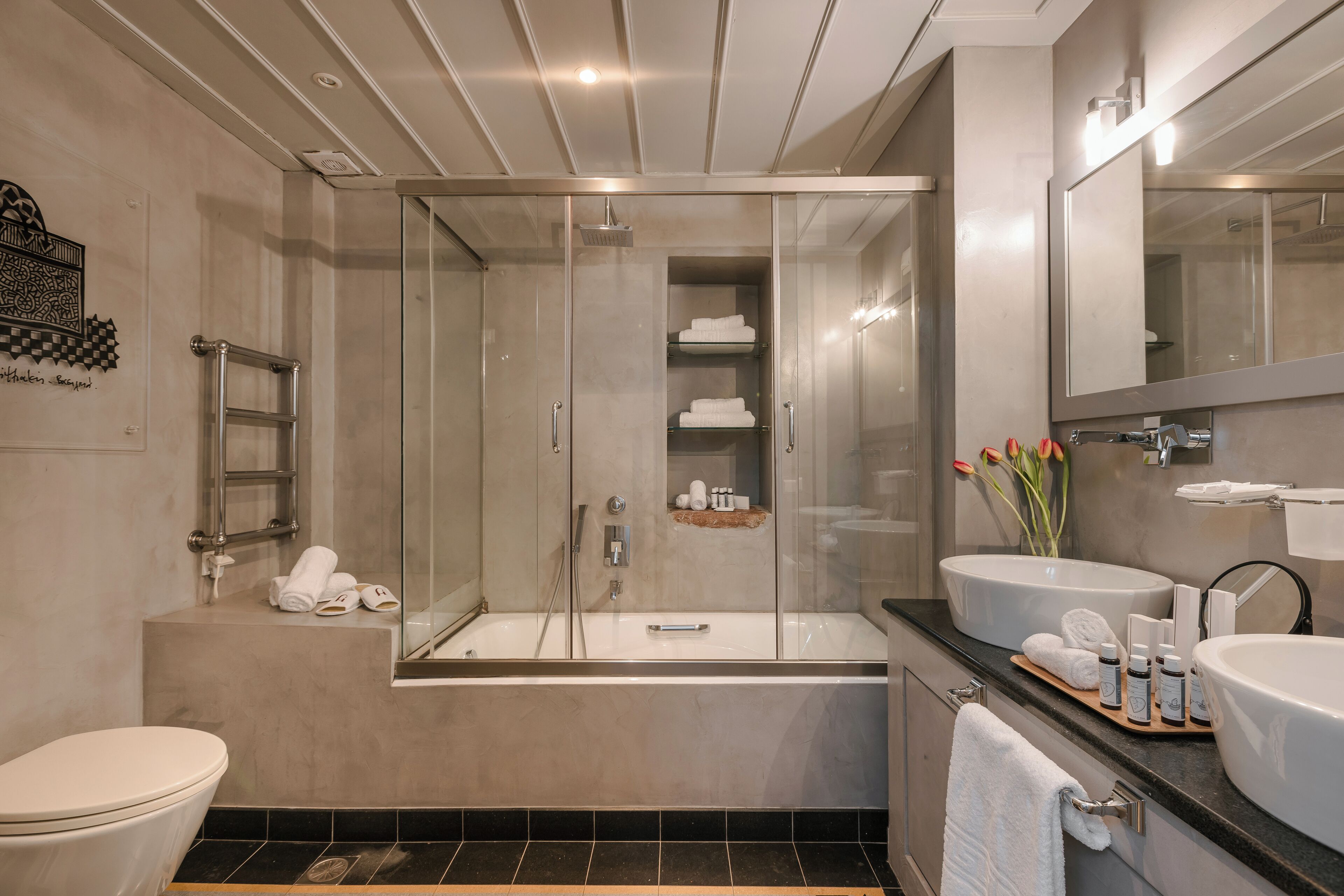 A modern bathroom with a glass-enclosed shower, a bathtub, two sinks, and a toilet.